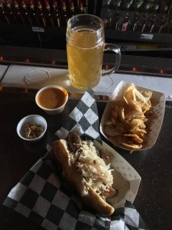 Mug of beer on frosty rail, homemade chips, bratwurst on pretzel bun with sauerkraut, whole-grain mustard and beer cheese on the side